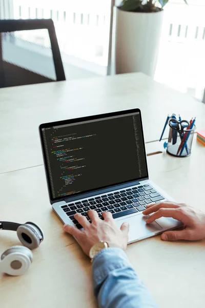 Vista parcial del desarrollador utilizando un ordenador portátil cerca de los auriculares en la mesa en el espacio de coworking - foto de stock