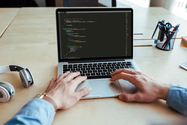 Vue partielle des mains masculines avec ordinateur portable près des écouteurs à table dans l'espace de coworking — Photo de stock