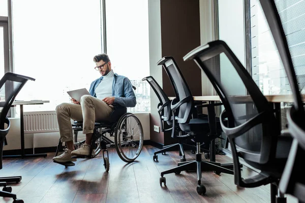 Concentration sélective du travailleur informatique handicapé sur le travail en fauteuil roulant avec ordinateur portable près des fenêtres dans l'espace de coworking — Photo de stock