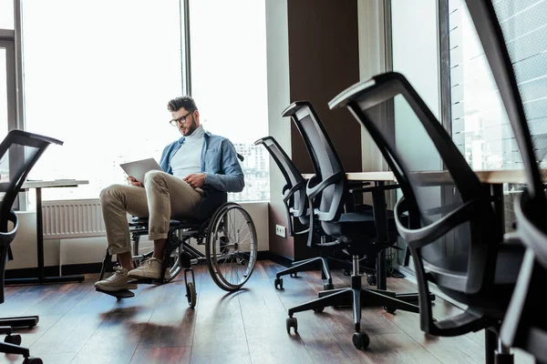 Selective focus of disabled IT worker on wheelchair working with laptop near windows in coworking space — Stock Photo