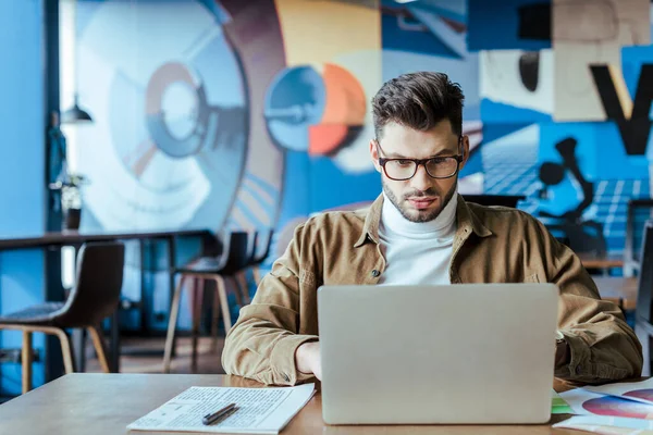 IT-Mitarbeiter mit Laptop in Zeitungnähe mit Stift am Tisch im Coworking Space — Stockfoto