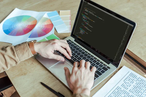 Vista recortada del desarrollador que trabaja con el ordenador portátil cerca de periódico, bolígrafo y papeles en la mesa en el espacio de coworking - foto de stock