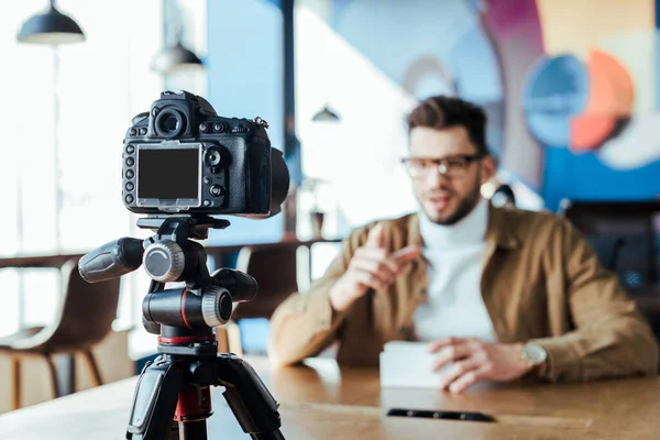 Selective focus of blogger in front of digital camera at table in coworking space — Stock Photo