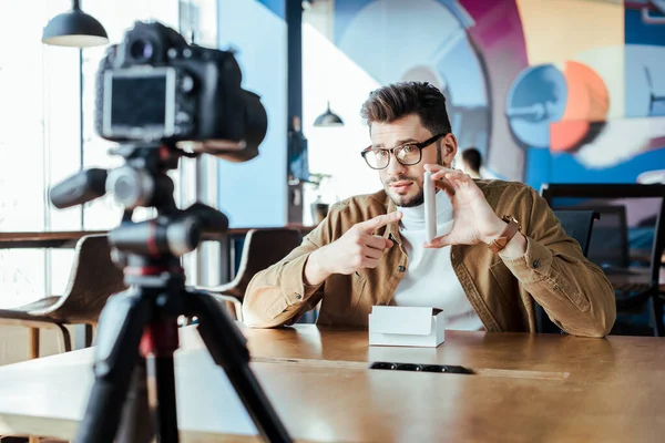 Selective focus of blogger in front of digital camera pointing on smartphone at table in coworking space — Stock Photo