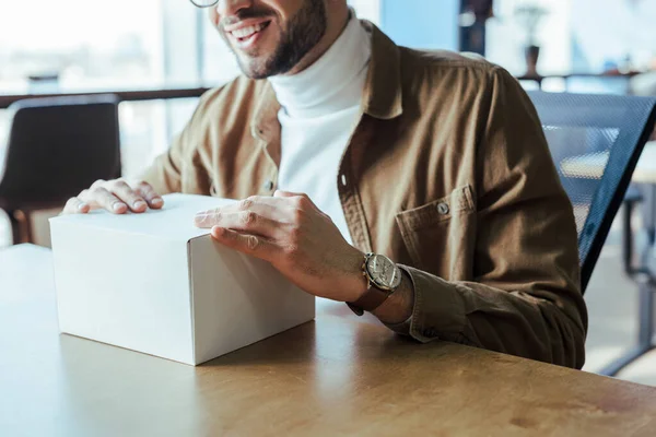 Vista ritagliata di blogger con scatola bianca sorridente a tavola nello spazio di coworking — Foto stock