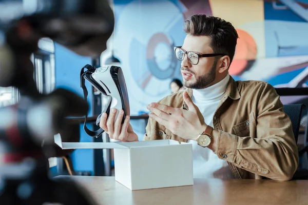 Selective focus of blogger pointing at virtual reality headset near box at table in coworking space — Stock Photo