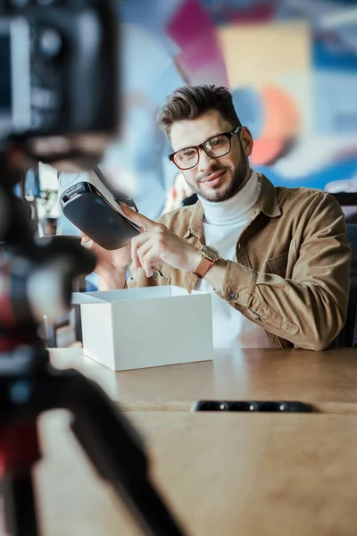 Selective focus of blogger pointing at virtual reality headset and smiling at table in coworking space — Stock Photo