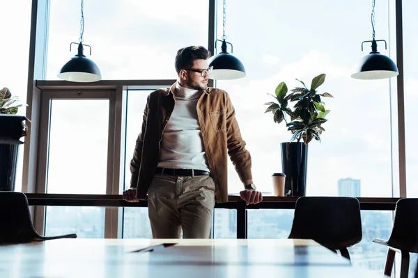 IT worker looking away at table with paper cup of coffee and flowerpot near windows — Stock Photo