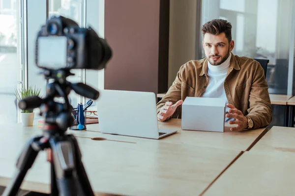 Selective focus of blogger with box near laptop at table in front of digital camera — Stock Photo