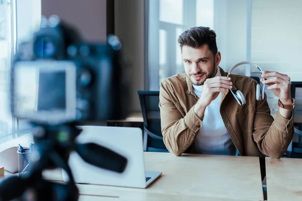 Selective focus of blogger showing headphones in front of digital camera in coworking space — Stock Photo