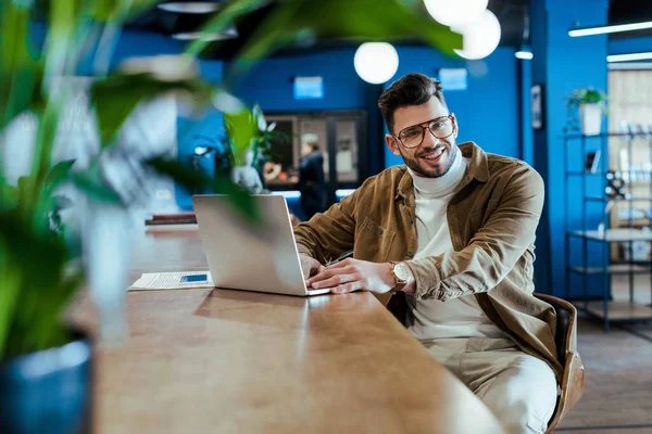 Selective focus of IT worker with laptop smiling in coworking space — Stock Photo