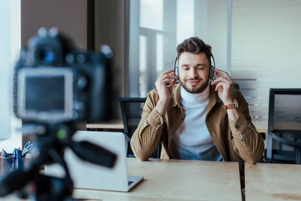 Selective focus of blogger with closed eyes in headphones listening music in front of digital camera — Stock Photo