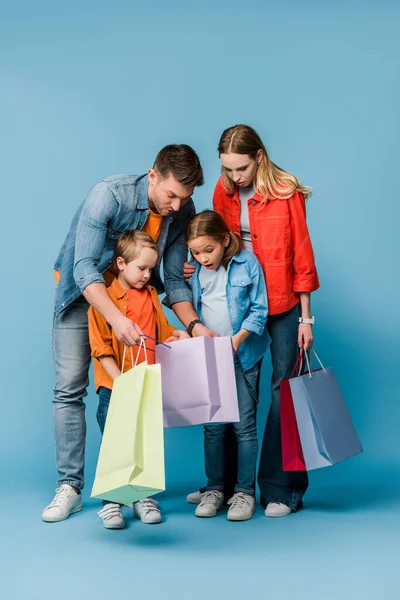Pais e crianças chocadas olhando em sacos de compras em azul — Fotografia de Stock
