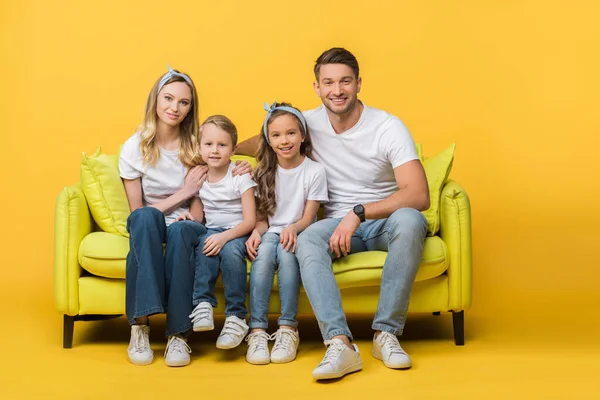 Happy family sitting together on sofa on yellow — Stock Photo