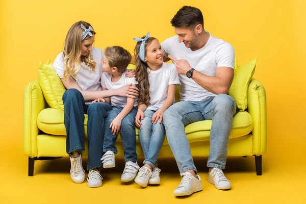 Glückliche Eltern im Gespräch mit Kindern, während sie zusammen auf dem Sofa auf gelb sitzen — Stockfoto