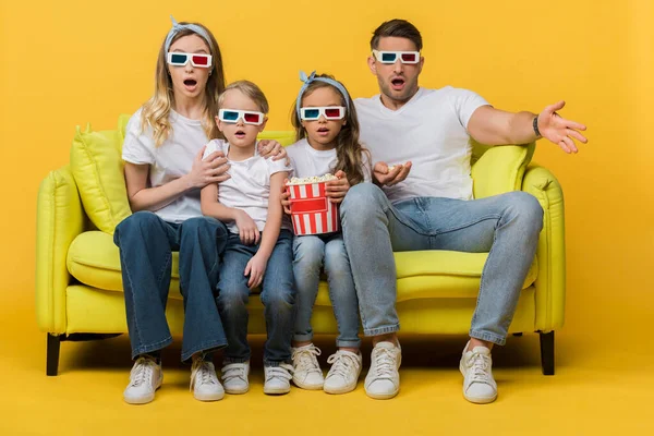 Familia conmocionada en gafas 3d viendo la película en el sofá con palomitas de maíz cubo en amarillo — Stock Photo
