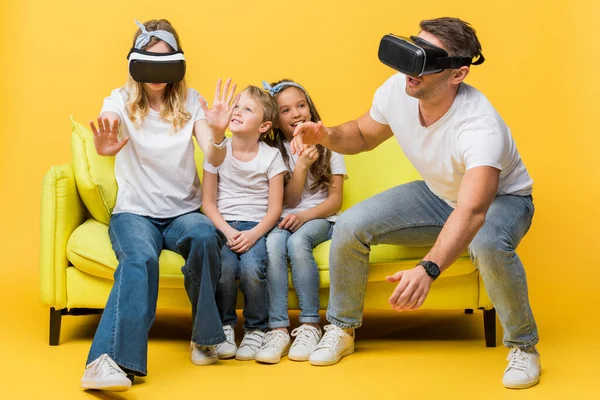 Smiling kids sitting on sofa with parents in virtual reality headsets on yellow — Stock Photo