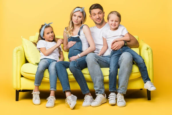 Mãe grávida feliz, pai e filhos sentados no sofá no amarelo — Fotografia de Stock