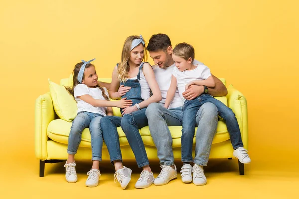 Emotionale schwangere Frau, Mann und Kinder sitzen auf dem Sofa auf gelb — Stockfoto