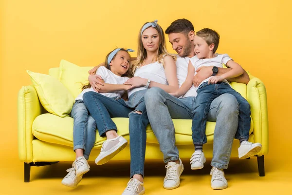 Sorrindo mãe grávida, pai e filhos sentados no sofá no amarelo — Fotografia de Stock