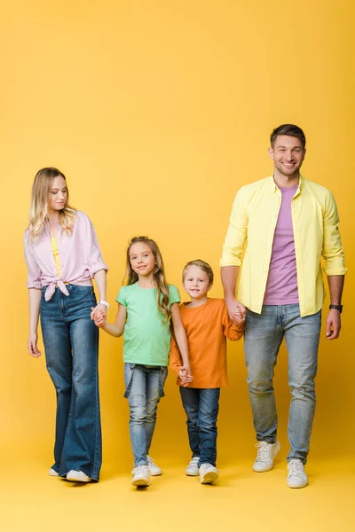 Happy parents holding hands with kids on yellow — Stock Photo