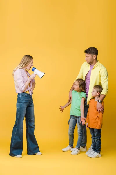 Angry mother yelling into megaphone on confused kids and husband on yellow — Stock Photo