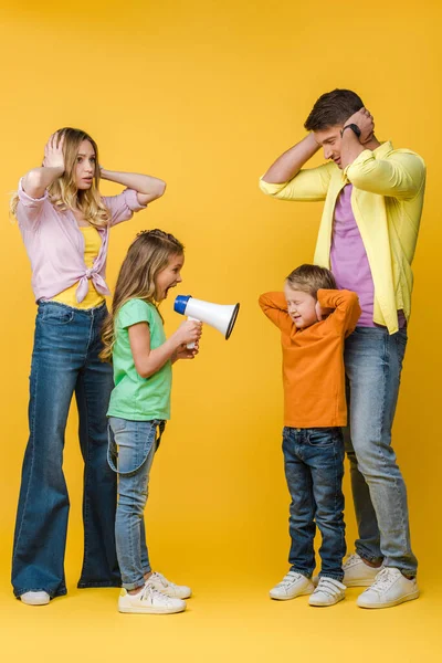 Fille criant dans mégaphone sur frère tandis que les parents ferment les oreilles sur jaune — Photo de stock