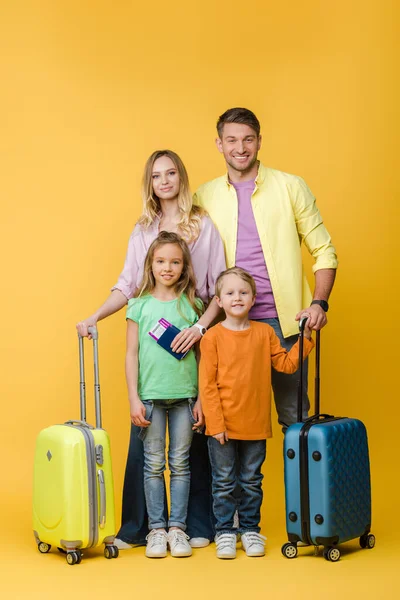 Familia sonriente de viajeros con equipaje, pasaportes y billetes en amarillo - foto de stock