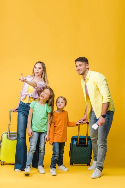 Glückliche Familie von Reisenden mit Gepäck, Pässen und Tickets, die auf gelb zeigen — Stockfoto