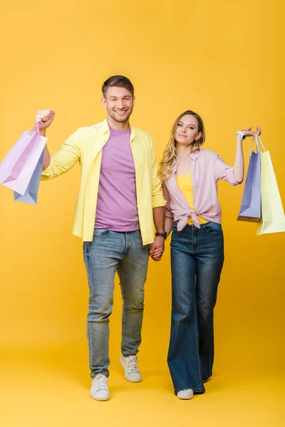 Beautiful smiling couple holding shopping bags on yellow — Stock Photo