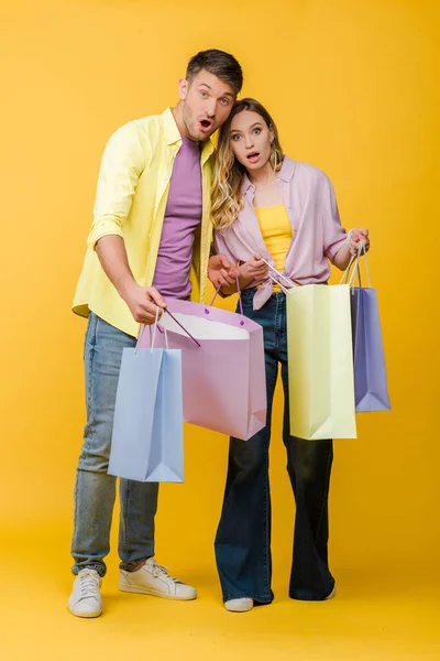 Belo casal surpreso segurando sacos de compras no amarelo — Fotografia de Stock