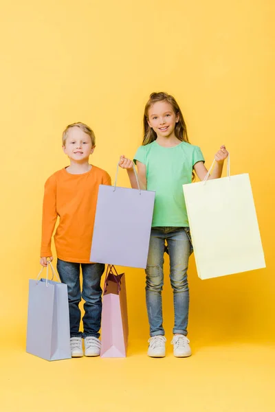 Adorable smiling kids holding shopping bags on yellow — Stock Photo