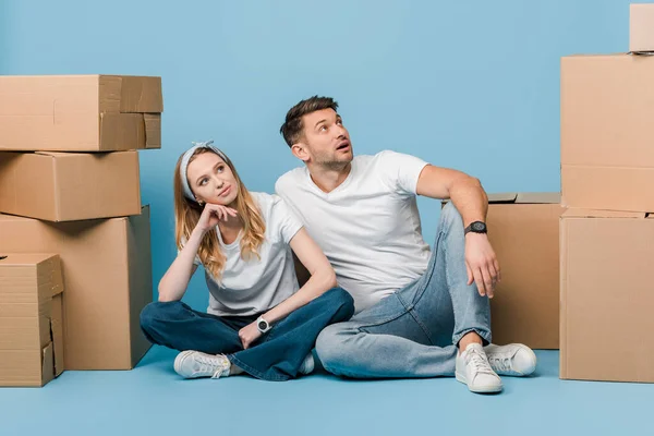 Мечтательная пара, сидящая с картонными коробками для перемещения на синий — стоковое фото
