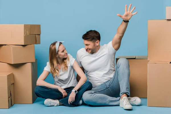 Excited couple sitting cardboard boxes for relocation on blue — Stock Photo