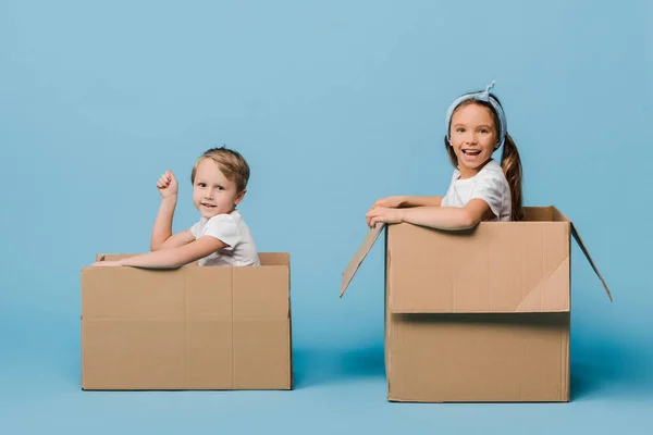 Adorable cheerful siblings playing in cardboard boxes on blue — Stock Photo