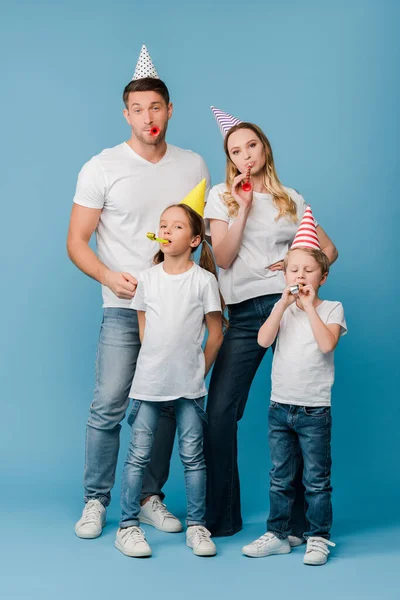 Familia feliz en gorras de fiesta de cumpleaños con sopladores en azul - foto de stock