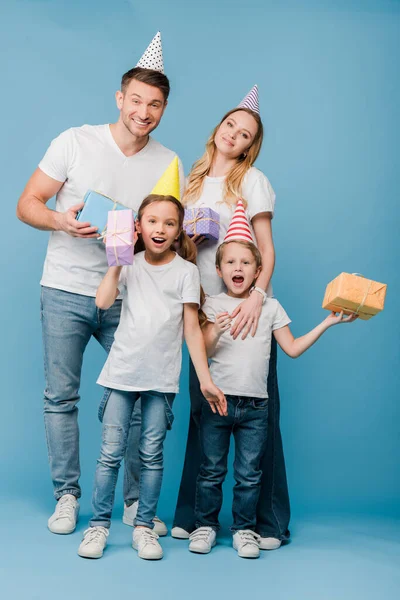 Excited parents and kids in birthday party caps holding gift boxes on blue — Stock Photo