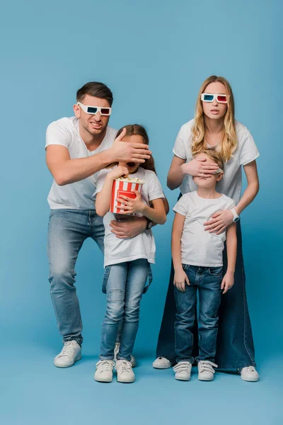 Шоковані батьки в 3d окулярах закривають очі дітям, що тримають попкорн на синьому — стокове фото