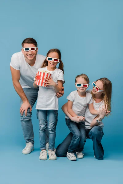 Щаслива сім'я дивиться фільм в 3d окулярах і тримає попкорн відро на синьому — стокове фото