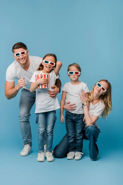 Gai famille regarder film en 3d lunettes et tenant seau de maïs soufflé sur bleu — Photo de stock