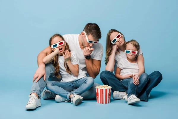 Confused family in 3d glasses watching movie and holding popcorn bucket on blue — Stock Photo