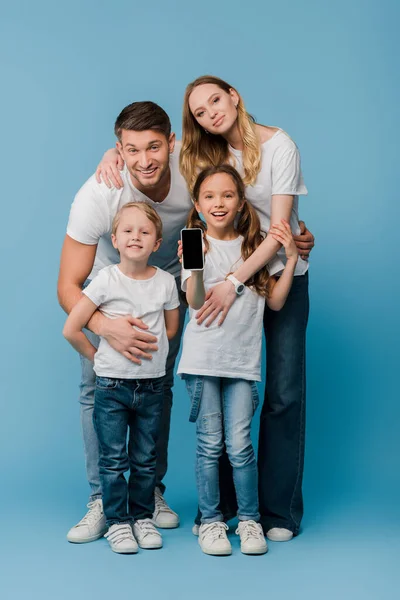Familia sonriente mostrando teléfono inteligente con pantalla en blanco en azul - foto de stock