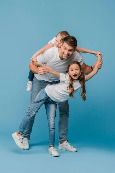 Smiling father piggybacking and plating with kids on blue — Stock Photo