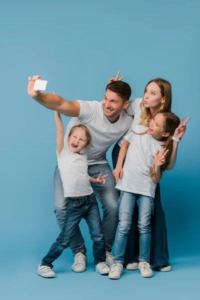 Cheerful family showing victory signs while taking selfie on smartphone on blue — Stock Photo