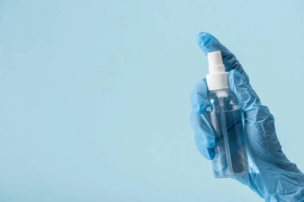 Vista recortada del médico en guante de látex que sostiene la botella con desinfectante de mano aislado en azul - foto de stock