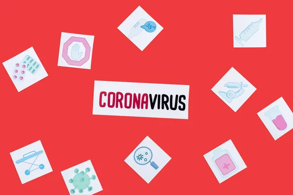 Top view of card with coronavirus lettering near drawn medical pictures isolated on red — Stock Photo