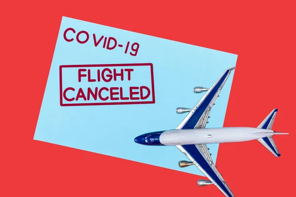 Top view of blue envelope with covid-19 and flight canceled lettering near toy airplane isolated on red — Stock Photo