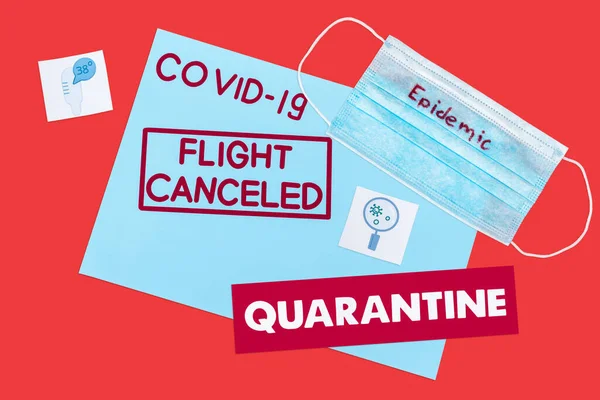 Top view of blue envelope with covid-19, flight canceled and quarantine lettering near medical mask and drawn medical pictures isolated on red — Stock Photo