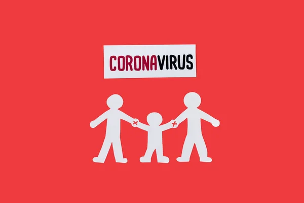 Top view of paper family with holding hands warning near coronavirus lettering isolated on red — Stock Photo