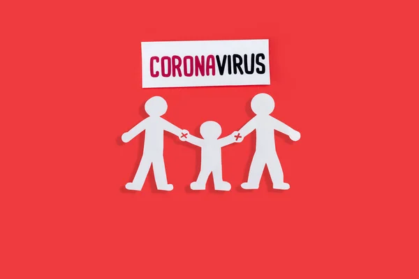 Vue du dessus des personnes en papier avec avertissement mains nues près de lettrage coronavirus isolé sur rouge — Photo de stock